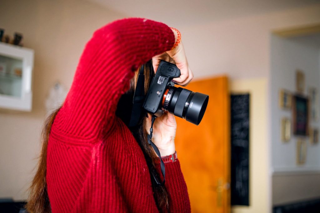 Frau im roten Pullover mit Kamera in der Hand