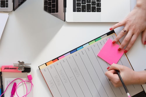 ein Planer mit einem pinken Post-It und einem Computer danben