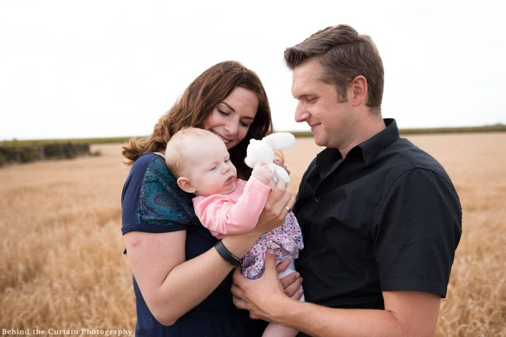 Mutter und Vater halten Kind im Arm und Kind spielt mit Kuscheltier
