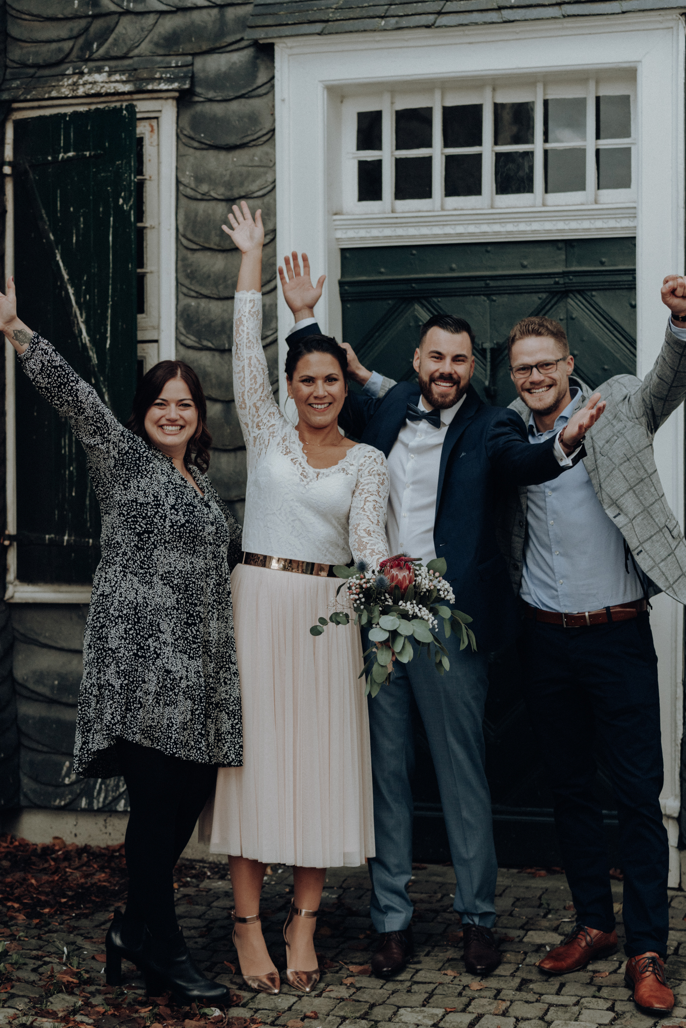 DSC08719_kleiner Hochzeitspaar steht mit Freunden vorm Standesamt und streckt die Hände in die Luft