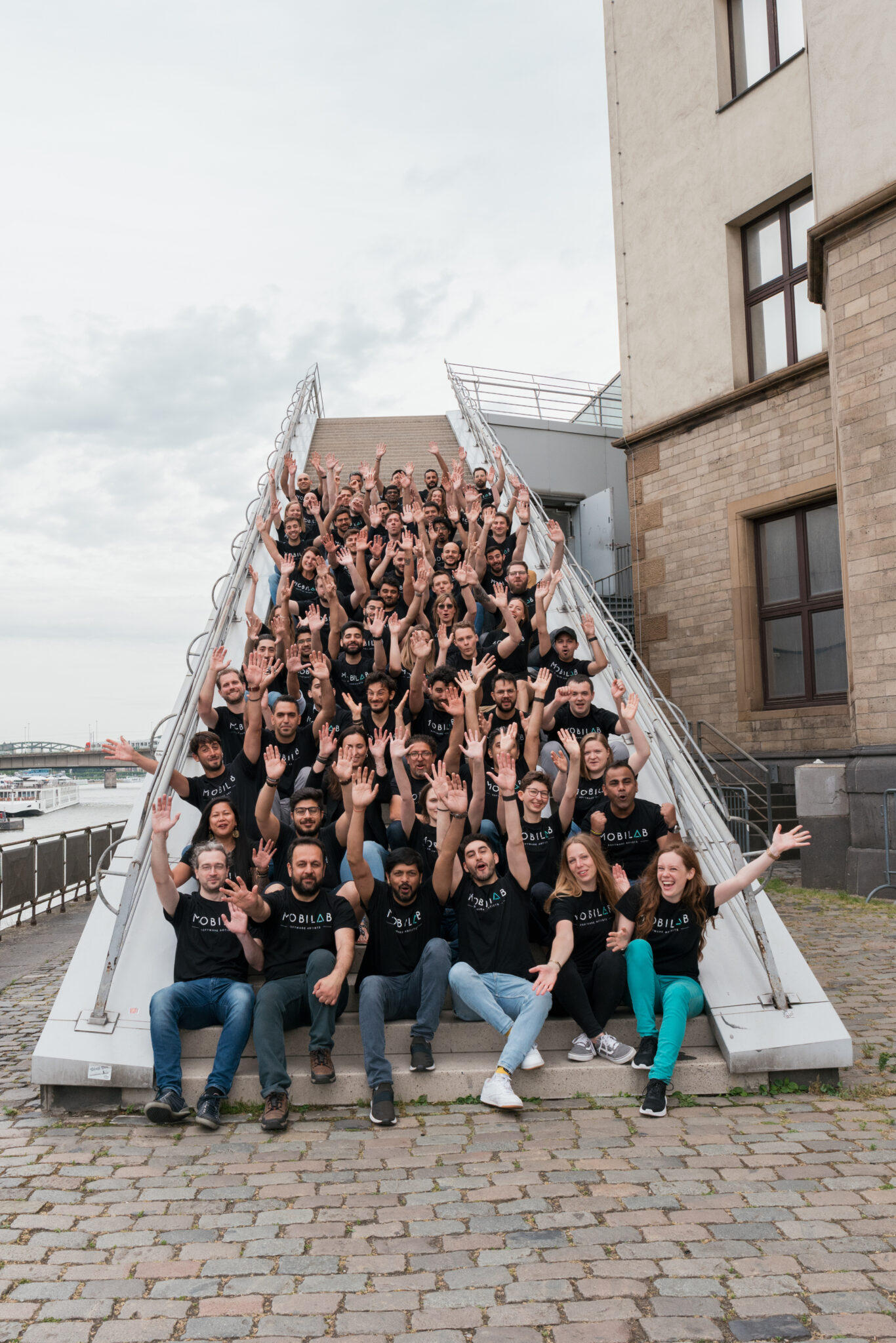 73R01302 Das ganze team eines Unternehmens sitzt auf einer Treppe und halten die Arme in die Höhe