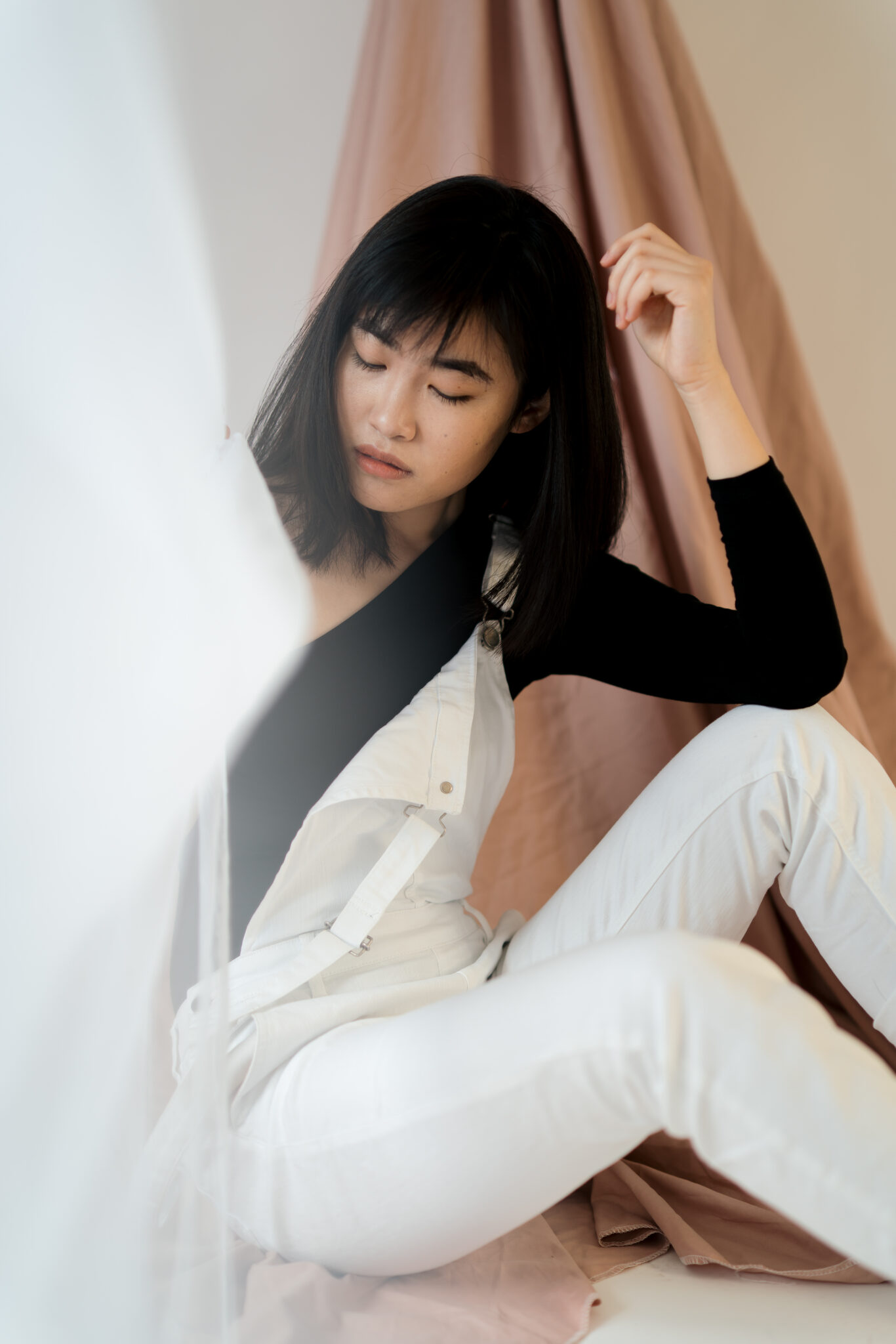 73R06253-15 Asiatische Frau sitzt zwischen Gardinen und schaut zum Boden