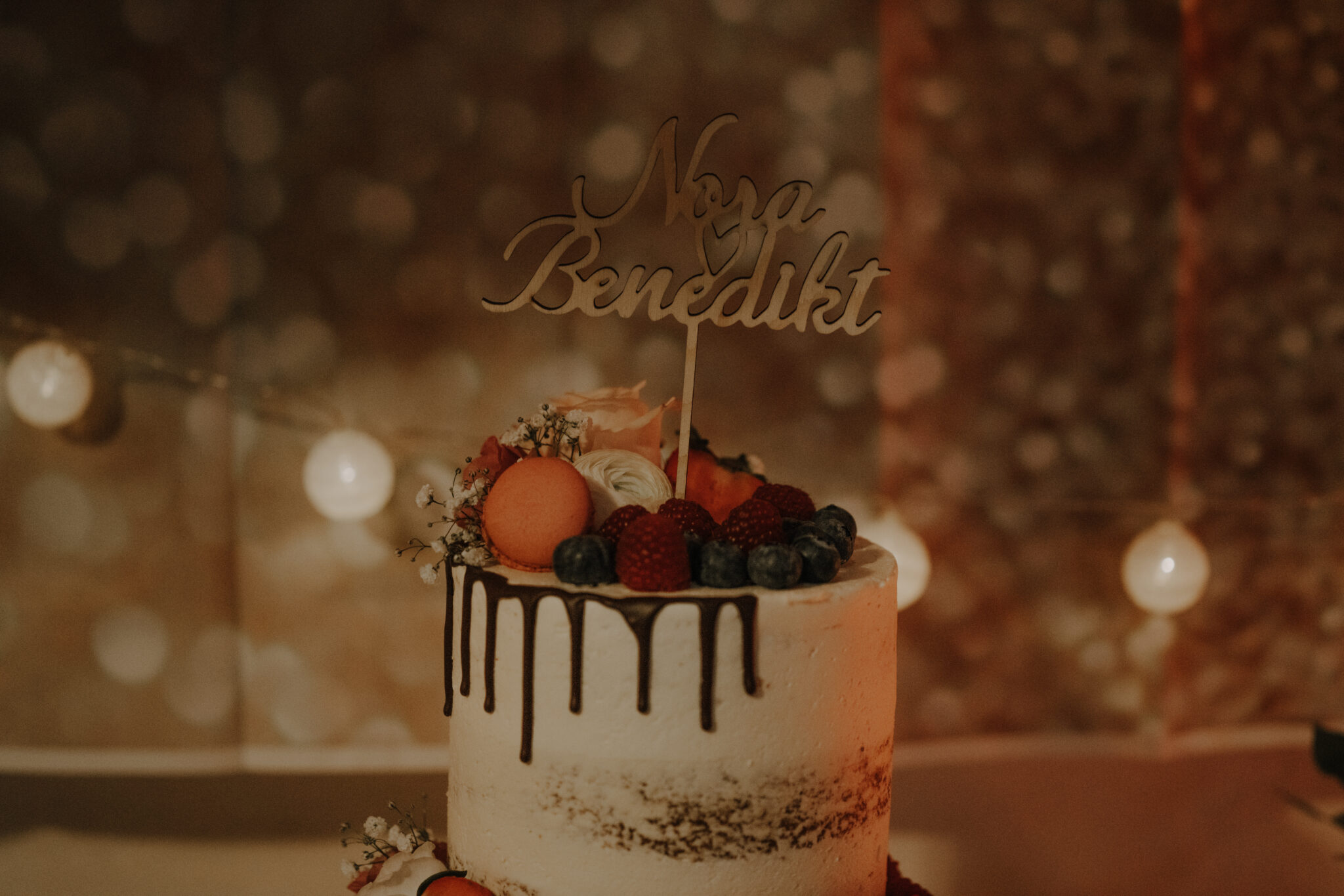 73R05497-2 Nahaufnahme Hochzeitstorte, goldener Einstecker Nora & Benedikt, Lichterketten, dämmrig, Erdbeeren, Schokolade