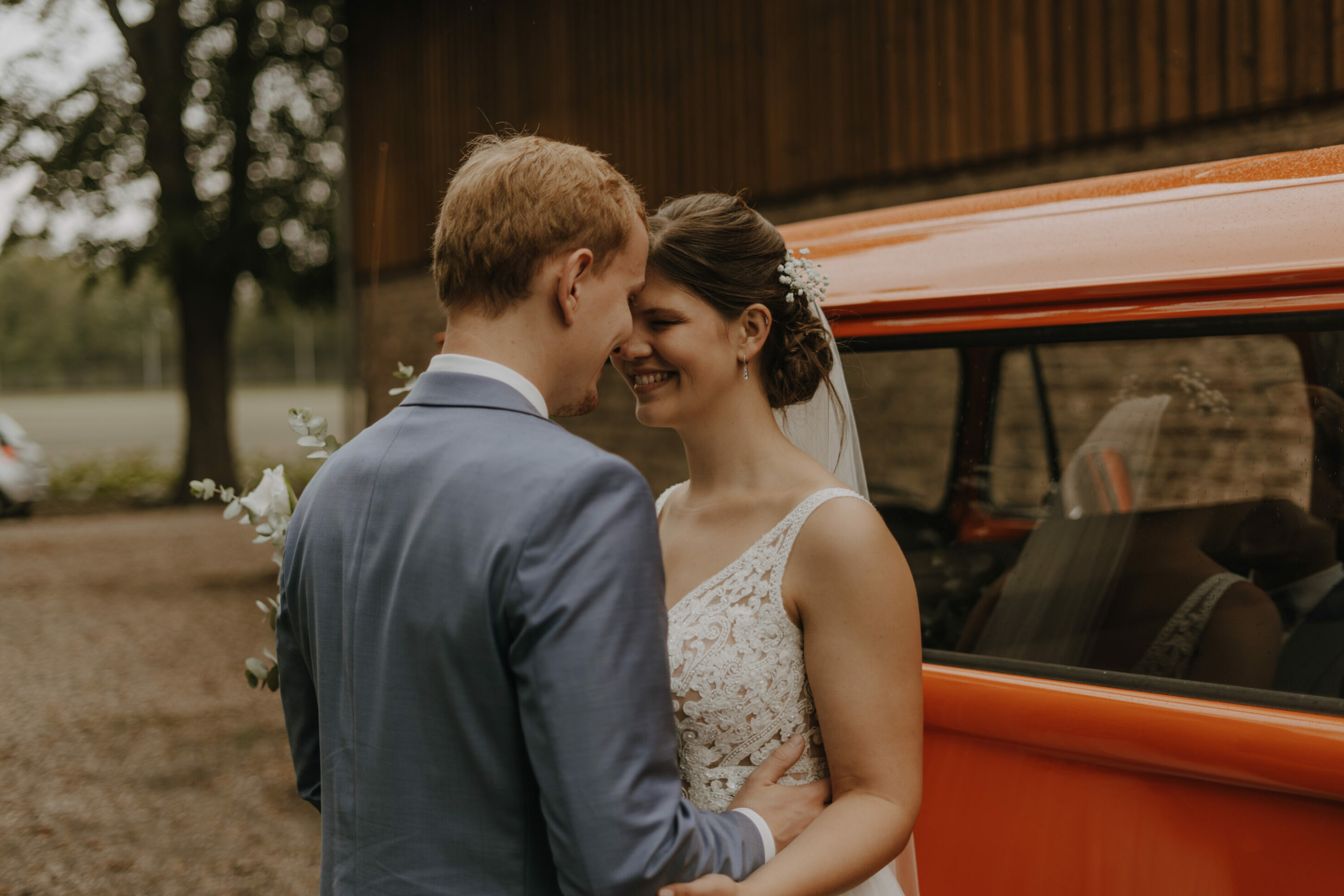73R03645-Inaundniklaskirchlich Brautpaar steht glücklich am Hochzeitsauto