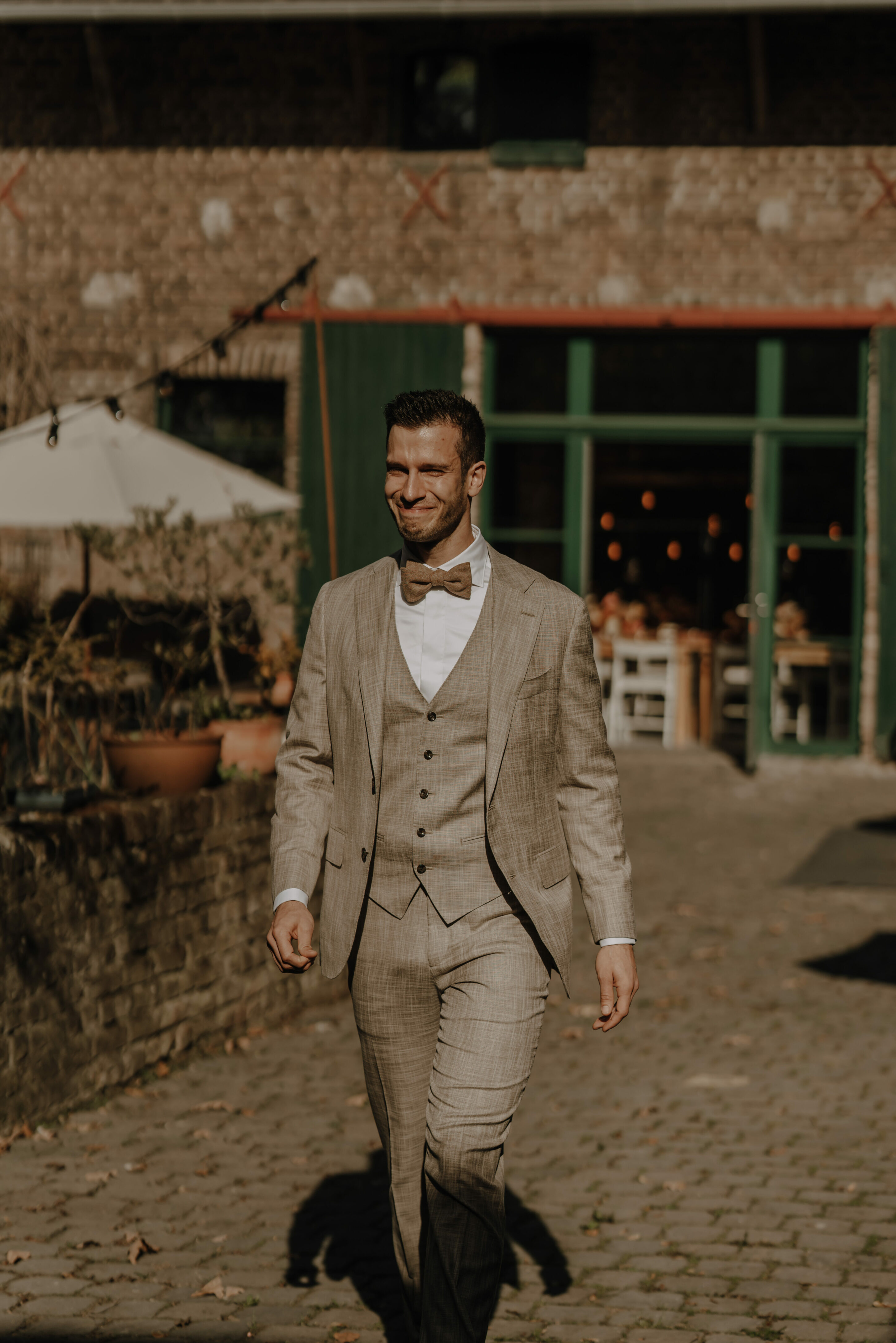 73R03695-annaundmarkhochzeit-3 Bräutigam läuft in sonnigem Innenhof freudig lächelnd & gerührt auf Braut zu