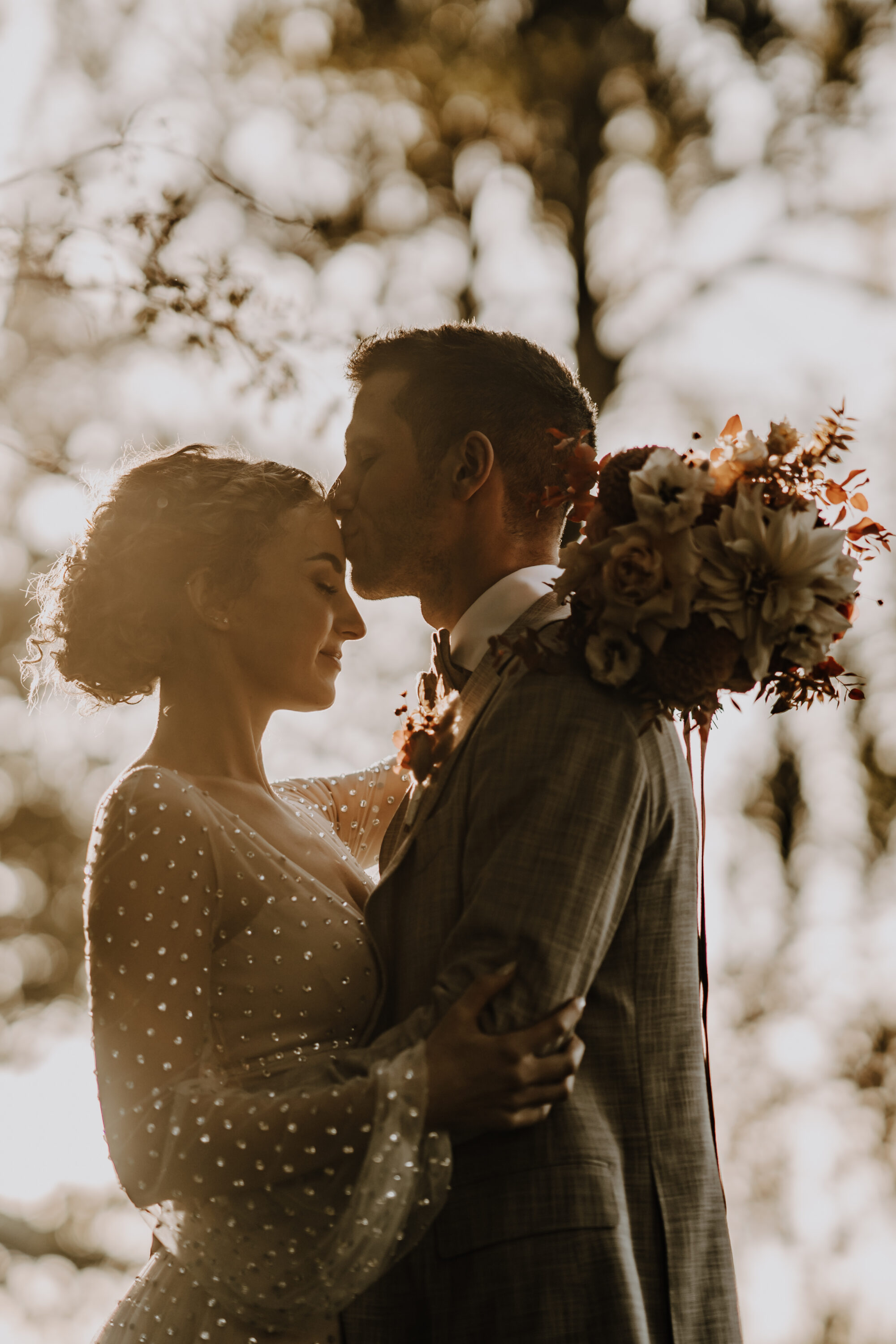 73R07422-annaundmarkhochzeit-3 Hochzeitspaar, sich im Arm haltend, gegen Sonne, warmes Licht, Bräutigam küsst Braut auf Stirn