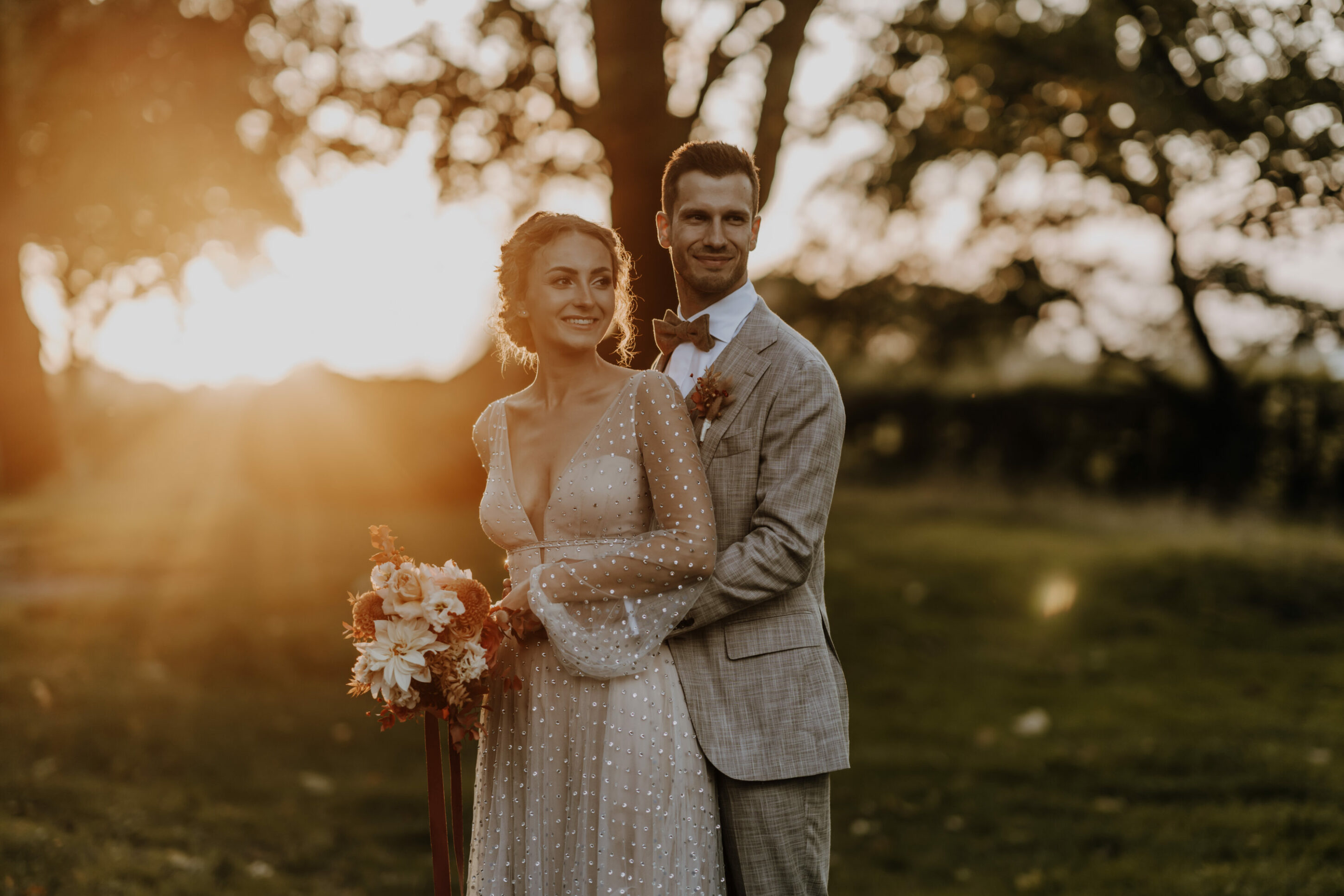 73R08196-annaundmarkhochzeit-4 Hochzeitspaar in Gegenlicht, Sonne, Sonnenuntergang, Glitzersteine auf Kleid, Brautstrauß