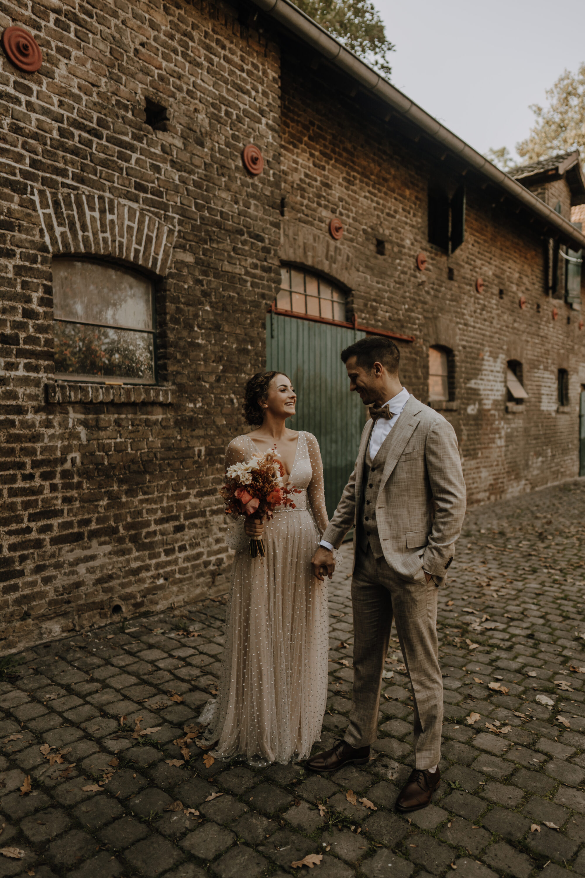 _74R3766-annaundmarkhochzeit-2 Brautpaar, Hand in Hand, lachend, im Innenhof