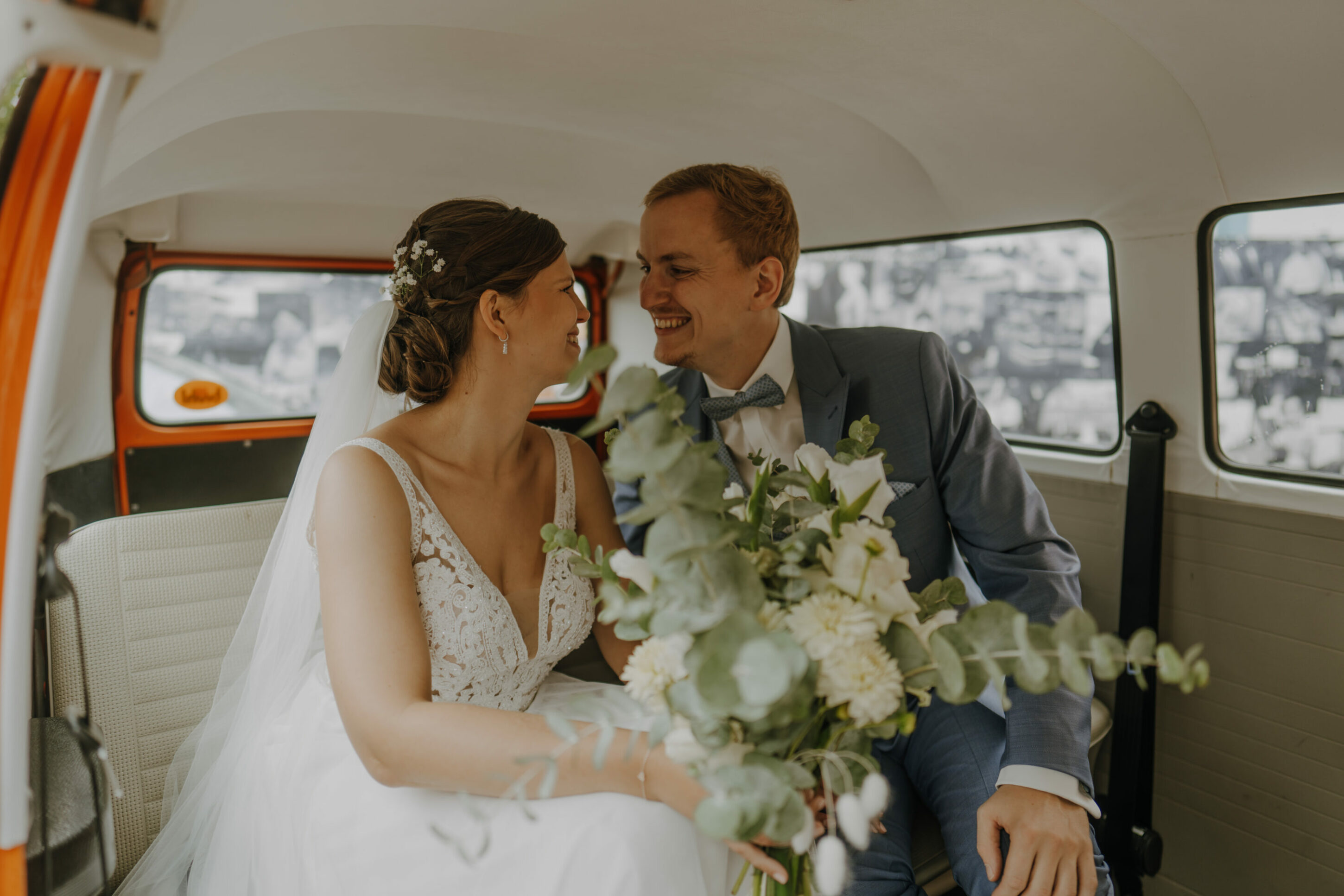 _74R7927-Inaundniklaskirchlich Hochzeitspaar sitzt glücklich in Hochzeitsauto, dem roten VW Bulli