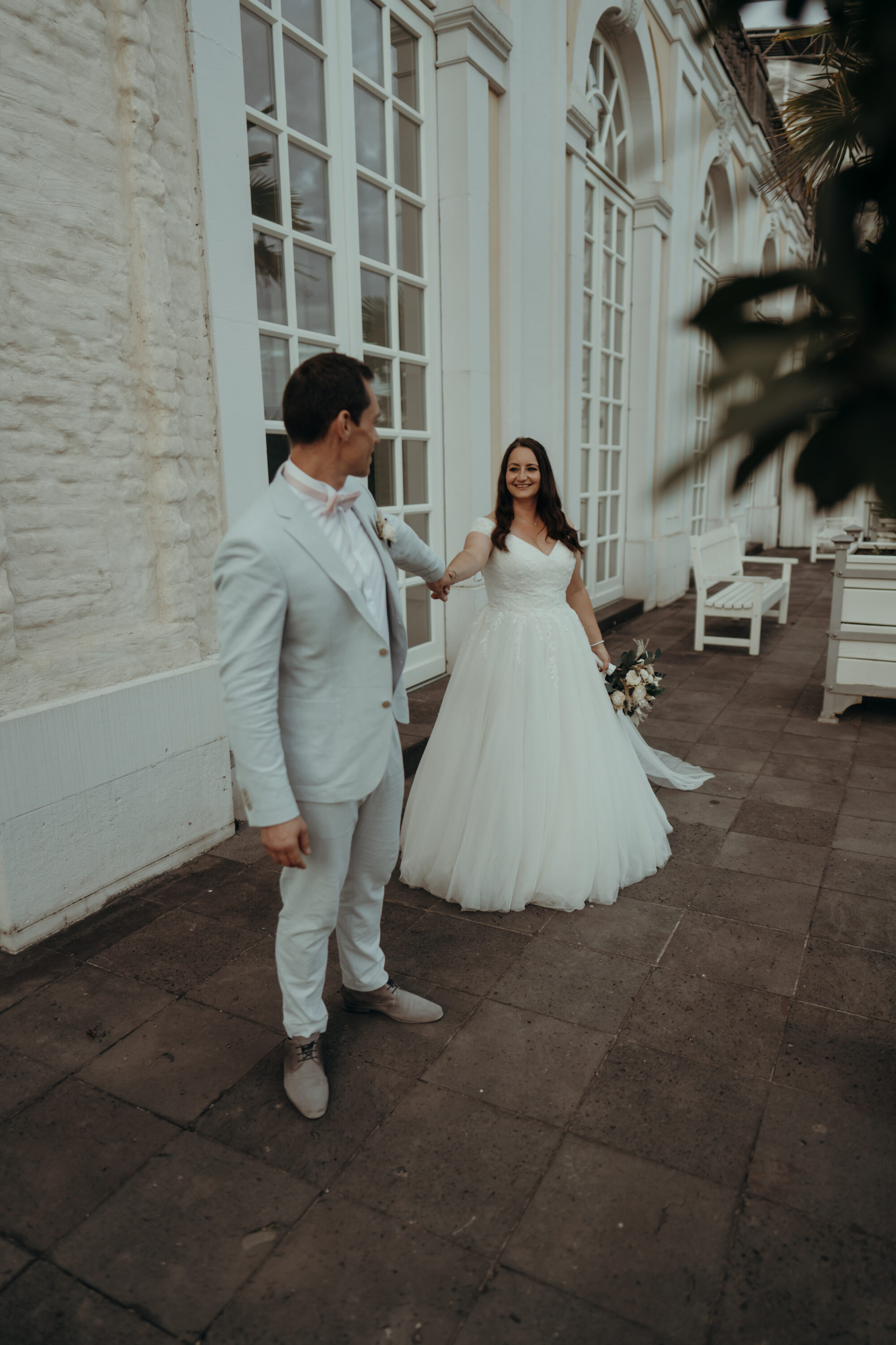 chrissandraafterwedding-6940-2 Kopie Braut und Bräutigam halten sich an der Hand, Bräutigam schaut nach hinten zur Braut, sie läuft ein Stück hinter ihm