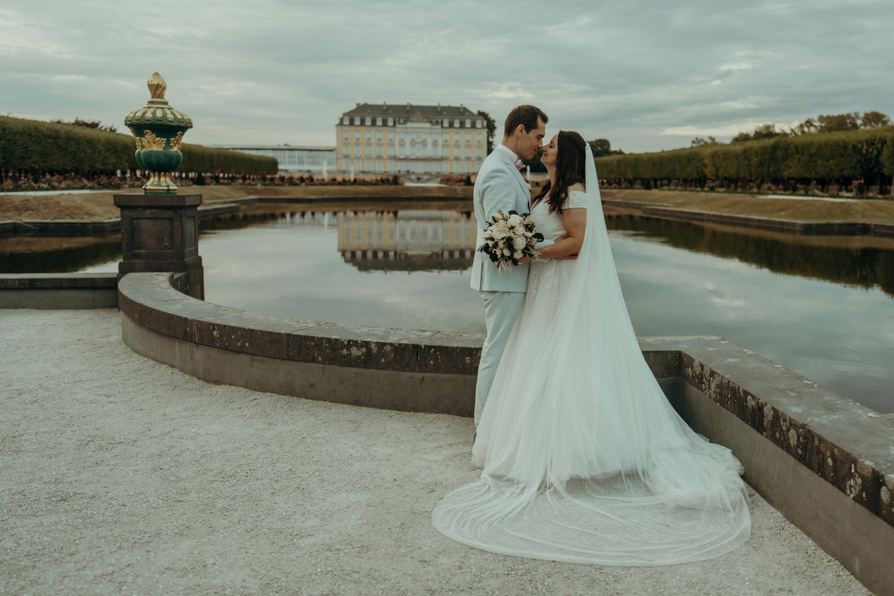 chrissandraafterwedding-7320-2 Kopie Brautpaar vor Schloss in der Ferne, Schlossteich in direktem Hintergrund, Paar Nasenspitzen aneinander, im Arm haltend